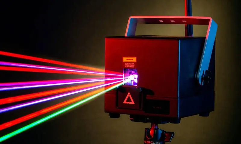 Lasercube laser projector closeup on a dark background with yellow halo around it, with laser lights projected out from the front.