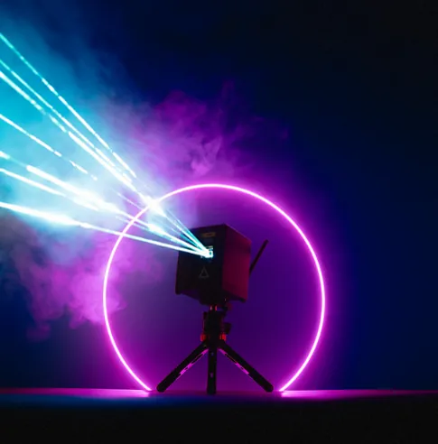 LaserCube WiFi on a tripod sending beams through haze, with a pink light ring behind it